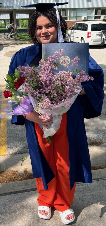 Mya holding her degree folder, a rose-centered bouquet, and a big bunch of purple lilacs